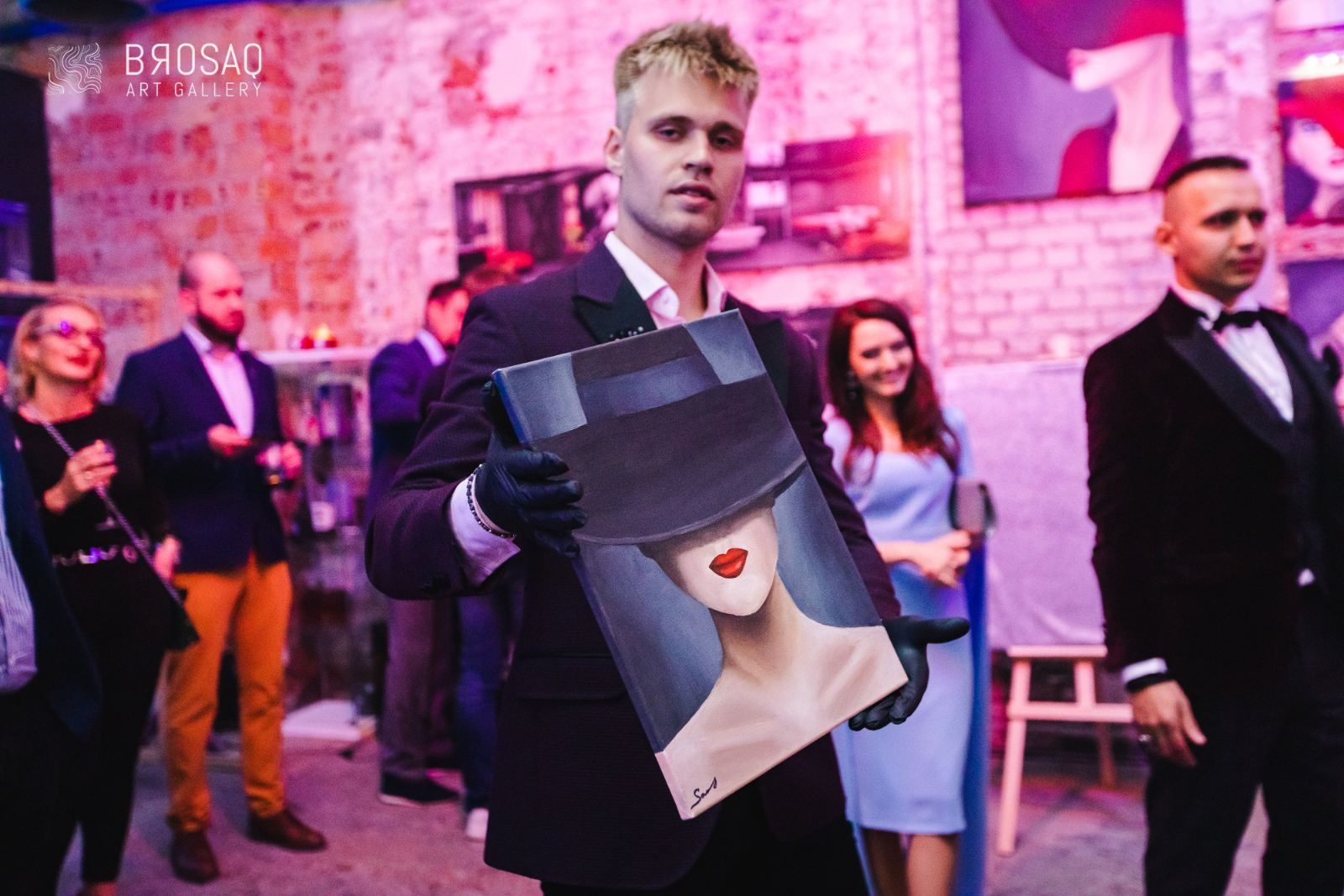 Goście oglądają obrazy na ceglanej ścianie galerii